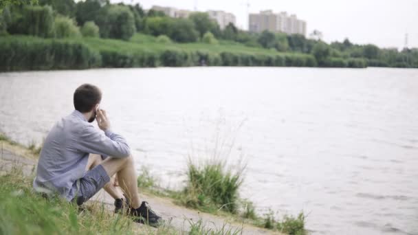 Ein Mann sitzt am Strand und telefoniert vor schönem Hintergrund — Stockvideo