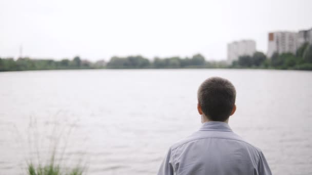 Ein Mann sitzt am Strand und blickt auf einen schönen Blick auf den Fluss in der Nähe des Parks — Stockvideo