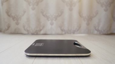 Kadın ayağı teraziye basıyor. Kadın odada vücut ağırlığını kontrol ediyor..