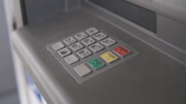 Bir adamın eli bir düğmeye basıyor ve bir ATM 'ye şifre giriyor.
