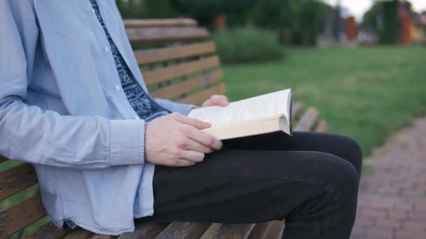 Un uomo seduto su una panchina in un parco e leggere un libro, voltando pagina — Video Stock