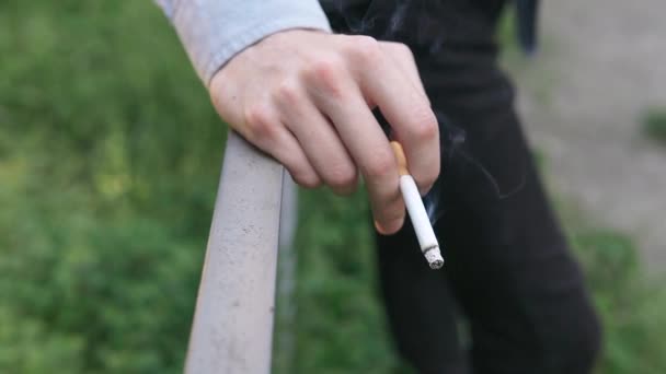 Joven sostiene un cigarrillo en sus manos y lo fuma — Vídeos de Stock