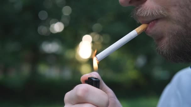 Бородатый человек курит сигарету на заднем плане вечерних огней города — стоковое видео