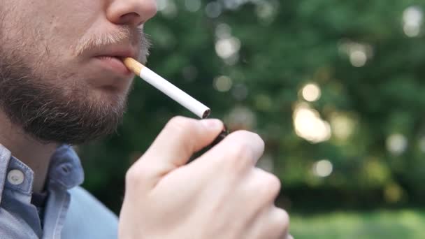 Mladý muž si zapálí cigaretu zblízka venku v parku — Stock video