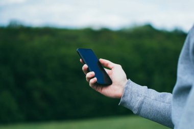 İnsan, doğanın arka planında akıllı telefonu tutarken kullanır.