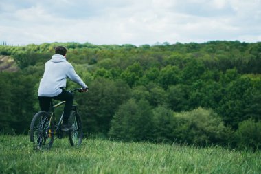 Bisiklet süren bir adam güneşli bir günde ormanın doğasına bakar.