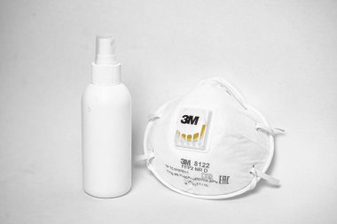 El ve yüzeyleri dezenfekte etmek için beyaz bir şişede COVID-19 dezenfekte edici virüslere karşı tek kullanımlık kumaş koruyucu yüz maskesi.