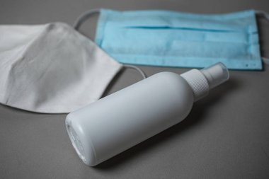 El ve yüzeyleri dezenfekte etmek için beyaz bir şişede COVID-19 dezenfekte edici virüslere karşı tek kullanımlık kumaş koruyucu yüz maskesi.