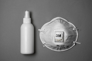 El ve yüzeyleri dezenfekte etmek için beyaz bir şişede COVID-19 dezenfekte edici virüslere karşı tek kullanımlık kumaş koruyucu yüz maskesi.