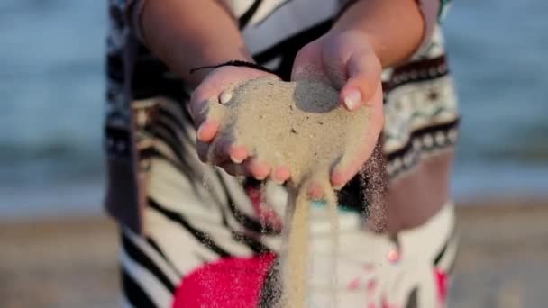 Weibliche Hand ergießt sich aus Sand am Meeresufer vor dem Hintergrund von Meereswellen — Stockvideo