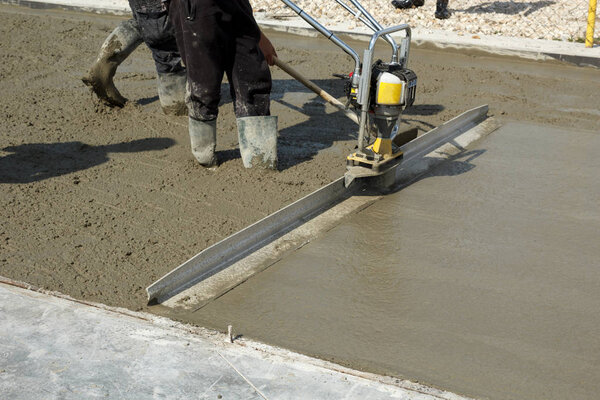 Smoothing concrete with gas powered vibrating screed machine