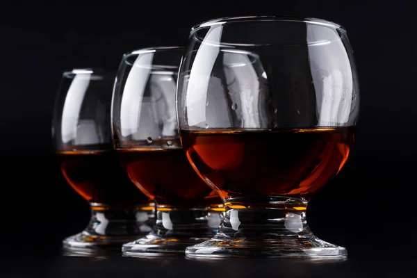 Drei Gläser mit Cognac hintereinander auf schwarzem Hintergrund — Stockfoto