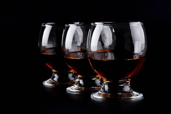 Three glasses with cognac in a row on a black background — Stock Photo, Image