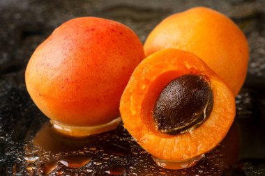 Kayısı meyve taze koyu arka plan üzerinde su damlaları ile yıkanmış taş, dilimlenmiş 2,5, yakın çekim