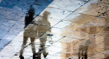 İki insan ve bir köpek ıslak kaldırımda bulanık yansıma gölgesi