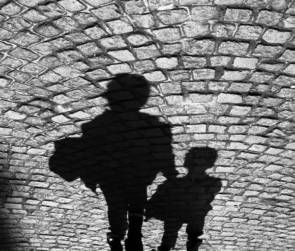 Shadow of an adult and a child on cobbled sidewalk