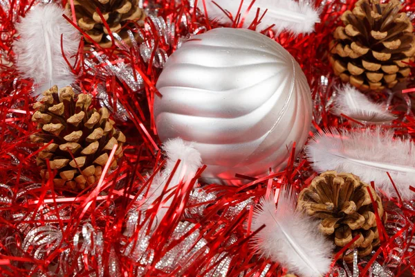 Çam kozalakları, tüy ve gümüşi Noel topu kırmızı bir süs üzerinde — Stok fotoğraf