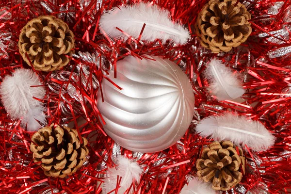 Conos de pinos, plumas y bolas de Navidad plateadas en un oropel rojo — Foto de Stock