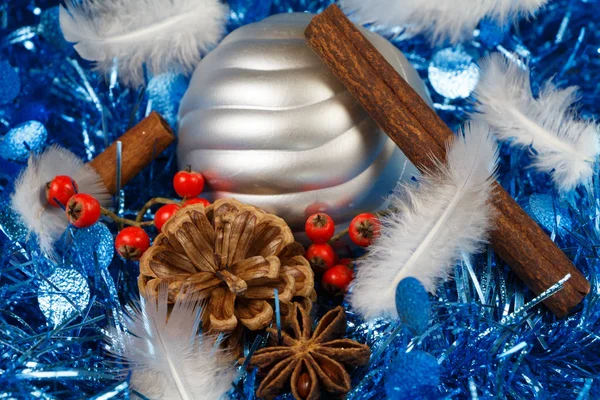 Çam kozalakları, tarçın çubukları, yıldız anasonu, tüy ve gümüşi bir Noel topu mavi bir süslemede. — Stok fotoğraf