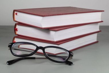 Bir yığın kırmızı kitap ve gözlük.