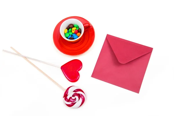 Oranje cup met kleurrijke knop-vormige chocolade, rode envelop en lollies. — Stockfoto