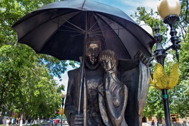 Bir erkek ve genç bir kız bir şehir sokak üzerinde bir şemsiye altında şehir heykel. 