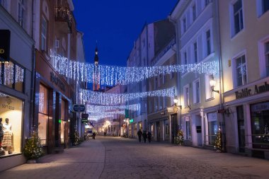 Tallinn, Estonya - 12 Ocak 2018: Arka planda mavi gökyüzü bulunan Tallinn 'in tarihi bölümünde Noel süslemeleri bulunan eski sokakların gece resmi kışı manzarası. 