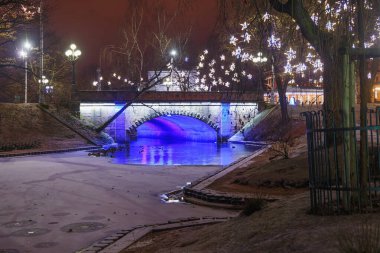 Riga 'daki Bastion Hill şehir parkında (Letonya) Alexander Köprüsü' nün gece manzarası. Köprü 1858-1859 yılları arasında inşa edildi ve 1902 yılında genişletildi..