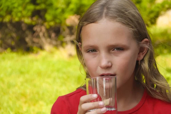 Little girl is drinking water from a glass in the nature — Stock Photo, Image