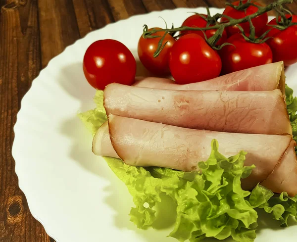 Mięso pokrojone w plastry pomidor sałata liść na białym talerzu drewniane — Zdjęcie stockowe