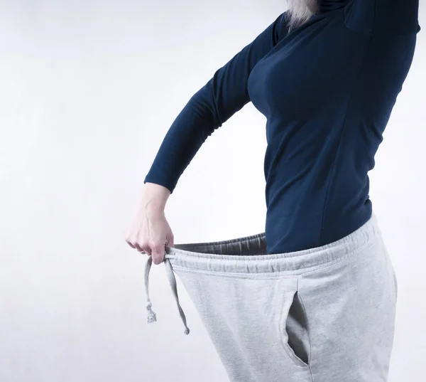 Женщина демонстрирует потерю веса, надевая старые большие штаны. Концепция потери веса — стоковое фото