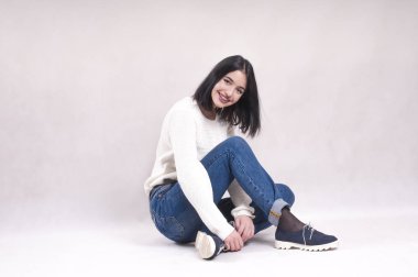 güzel kız kot pantolon katta oturur ve beyaz bir kazak diş teli