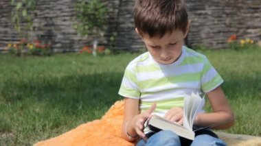 Çocuk çimlerin üzerine bir kitap okuyor