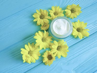 Mavi ahşap arka plan üzerinde kozmetik krem sarı çiçek