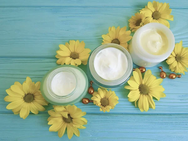 kozmetik krem sarı çiçekler mavi ahşap arka plan kapsül