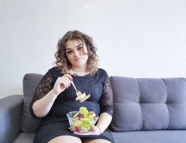 bir tabak salata ile kanepede oturan güzel tam uzunlukta kız