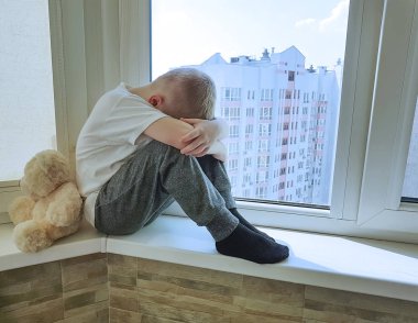 bir pencerede bir oyuncak ayı ile küçük üzgün çocuk oturur