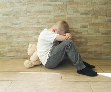 oyuncak ayı ile katta oturan küçük üzgün çocuk