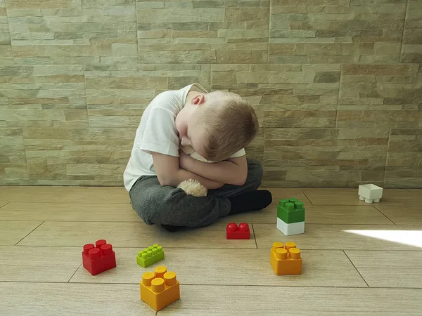 little sad boy sits on the floor with a block, teddy bear toy