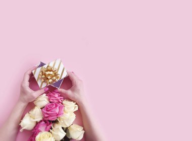 Bir hediye kutusu tutan kadın elleri, renkli bir arka planda bir buket gül.