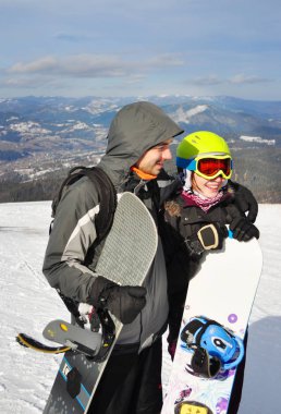 Bir kız ve bir erkek ayakta, gülümseyen ve snowboads tutarak 