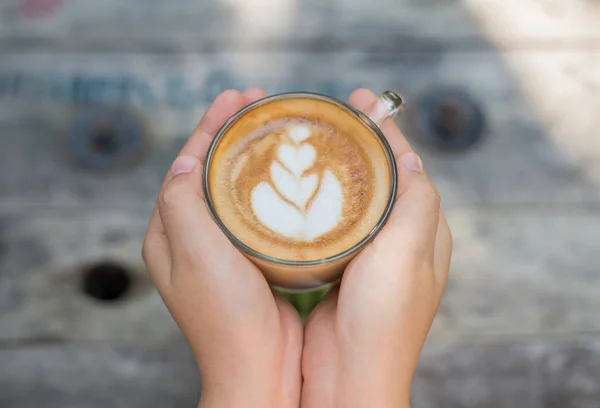 Weibliche Hände, die eine Tasse Kaffee über einem Holztisch halten, Draufsicht — Stockfoto