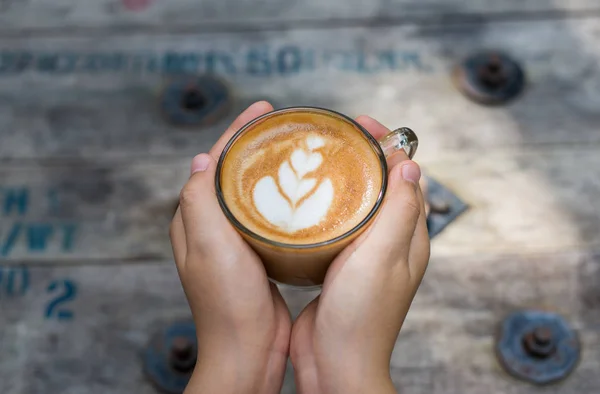 Weibliche Hände, die eine Tasse Kaffee über einem Holztisch halten, Draufsicht — Stockfoto