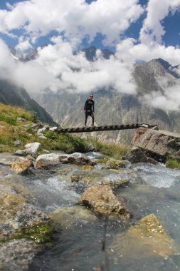 Kafkasya dağlarında yaz yürüyüşü: Yürüyüşçü köprü ve açık hava macera konsepti kullanarak hızlı akan dağ nehrini geçiyor