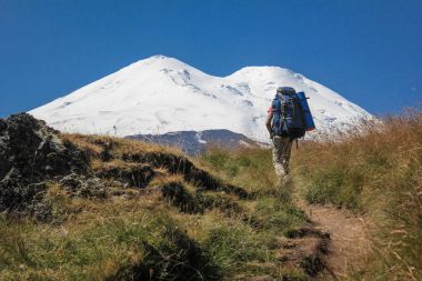 uzun yürüyüşe çıkan kimse bir sırt çantası ile dağlara tırmanmak. Elbrus yaz yükseliş