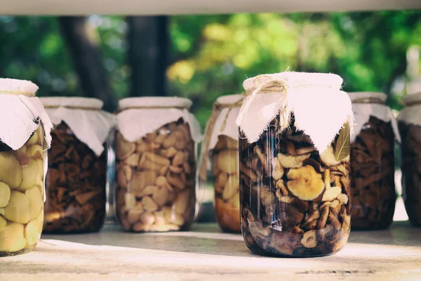 Cogumelos marinados deliciosos caseiros nos frascos de vidro na mesa. Frascos de vidro com cogumelos selvagens na mesa branca . — Fotografia de Stock