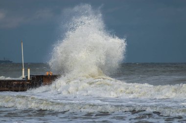 Fırtınalı havada dalgalı su ve liman. Büyük dalgalar rıhtıma çarpıyor. Küresel ısınmanın bir sonucu olarak orta enlemlerde anormal derecede güçlü fırtınalar meydana geliyor..