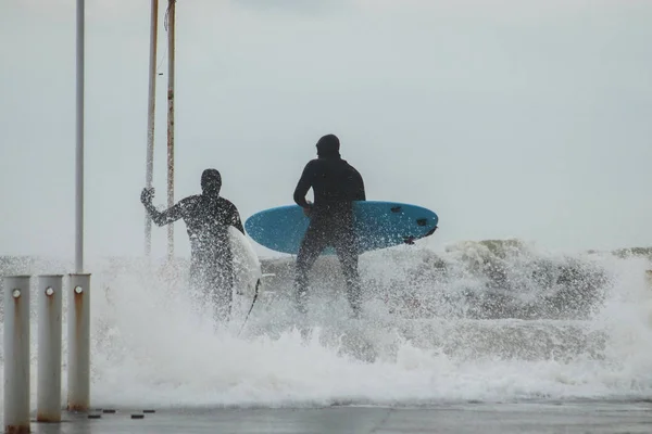 Avustralya 'da güçlü dalgaların ortasında sörf tahtasıyla bir şehir iskelesinde sörf yapan iki sörfçü. Kavram: Doğayla insan arasındaki çatışma, ekstrem sporlar ve hobiler, doğa insana karşı. Arka plan — Stok fotoğraf
