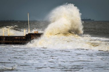 Fırtınalı havada dalgalı su ve liman. Büyük dalgalar rıhtıma çarpıyor. Küresel ısınmanın bir sonucu olarak orta enlemlerde anormal derecede güçlü fırtınalar meydana geliyor..