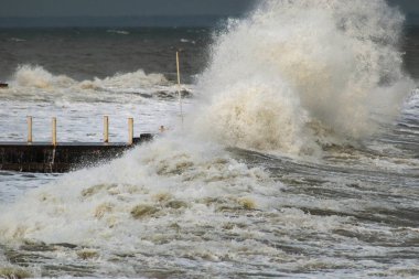 Fırtınalı havada dalgalı su ve liman. Büyük dalgalar rıhtıma çarpıyor. Küresel ısınmanın bir sonucu olarak orta enlemlerde anormal derecede güçlü fırtınalar meydana geliyor..